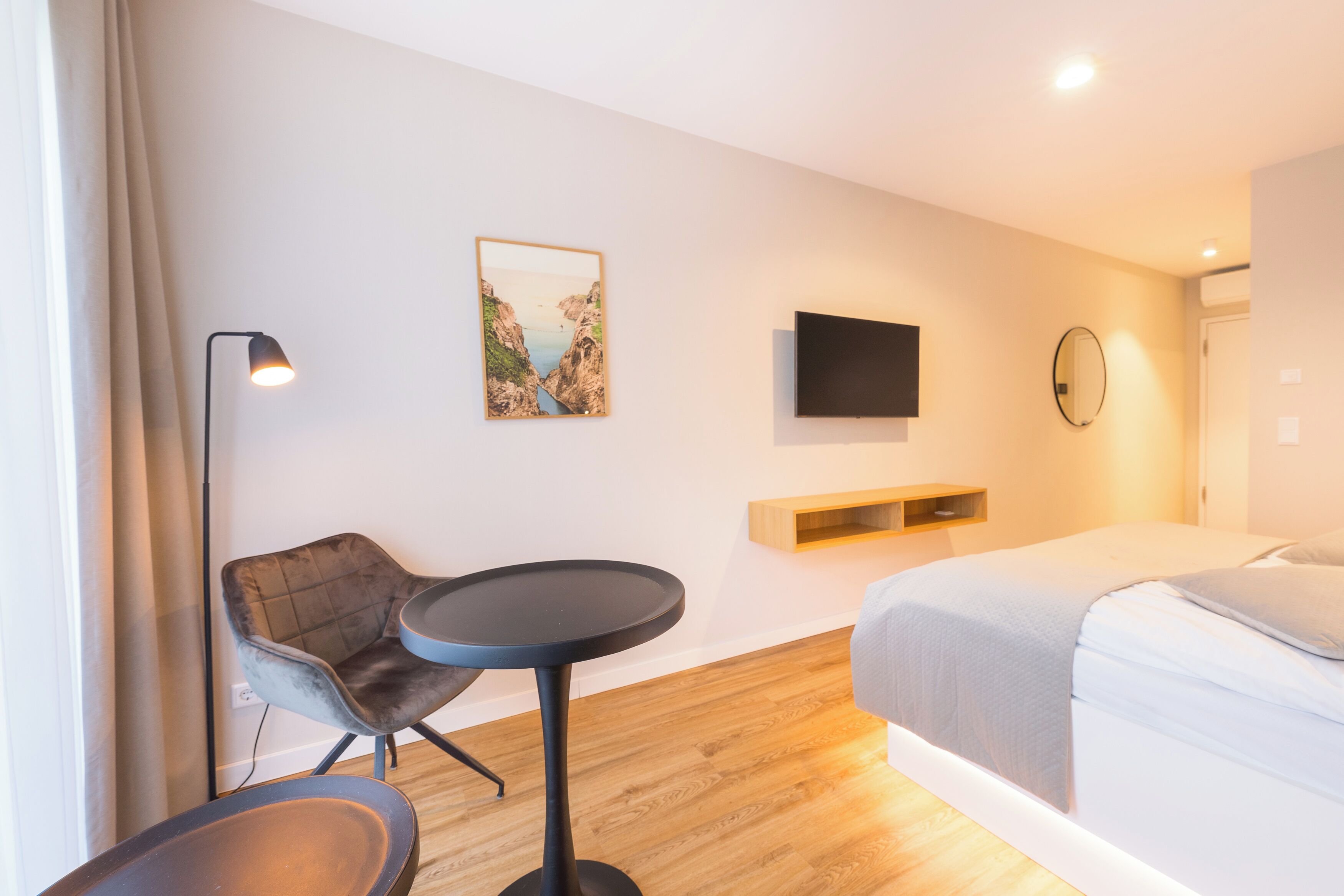 A modern hotel room with a bed, a desk, a chair, a TV, and a painting on the wall.