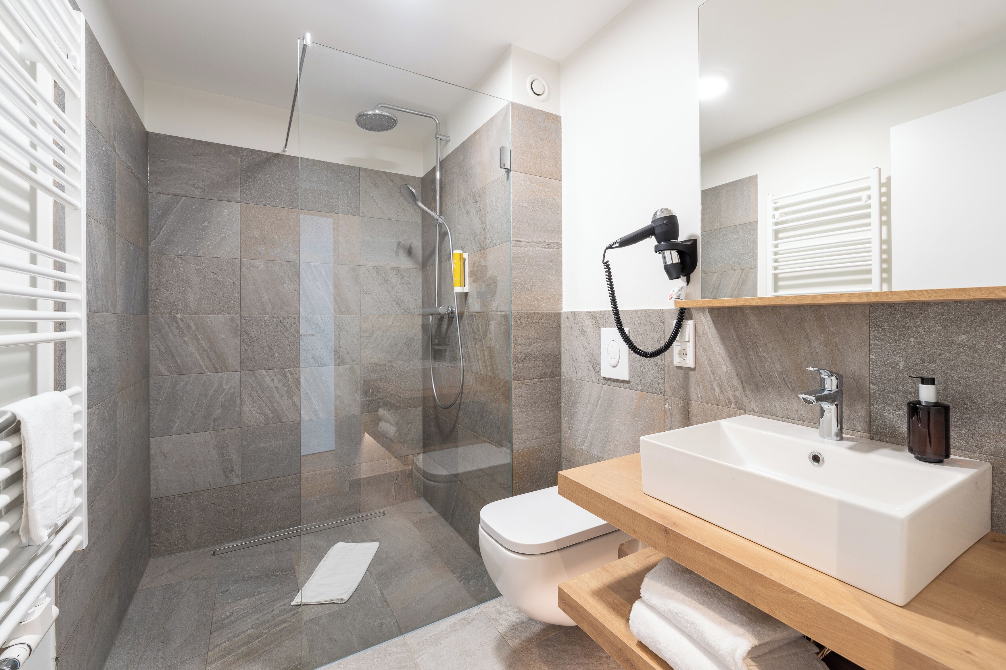 Un baño moderno con ducha envuelta en vidrio, un lavamanos blanco y un mueble de tocador de madera.
