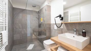 Un baño moderno con ducha envuelta en vidrio, un lavamanos blanco y un mueble de tocador de madera.