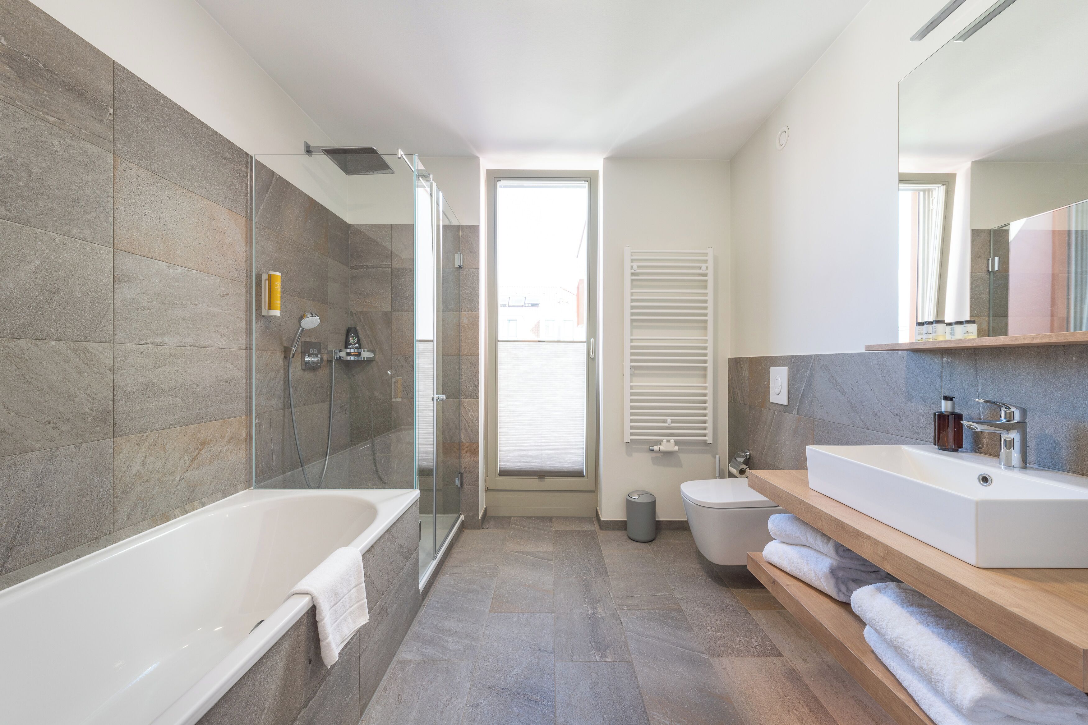 A modern bathroom with a glass-enclosed shower, a freestanding bathtub, a vanity with a large mirror, and a toilet.