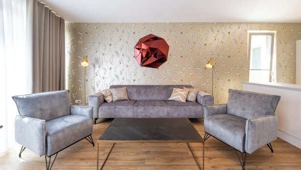 A modern living room with a grey sofa, two armchairs, a black coffee table, and a geometric wall decoration.