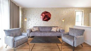 Una sala de estar moderna con un sofá gris, dos sillones, una mesa de centro negra y una decoración geométrica en la pared.