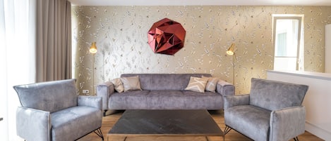 A modern living room with a grey sofa, two armchairs, a black coffee table, and a geometric wall decoration.