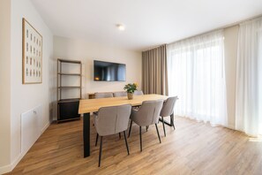 A dining area with a wooden table, grey chairs, a flat-screen TV, a plant, and a bookshelf. - Design Apartments - Luise (Potsdam)