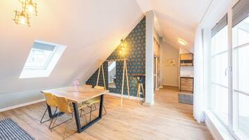 Ein modernes Schlafzimmer im Loft-Stil mit einem Oberlicht, einem Essbereich mit Holztisch und -stühlen sowie einer Küche im Hintergrund.