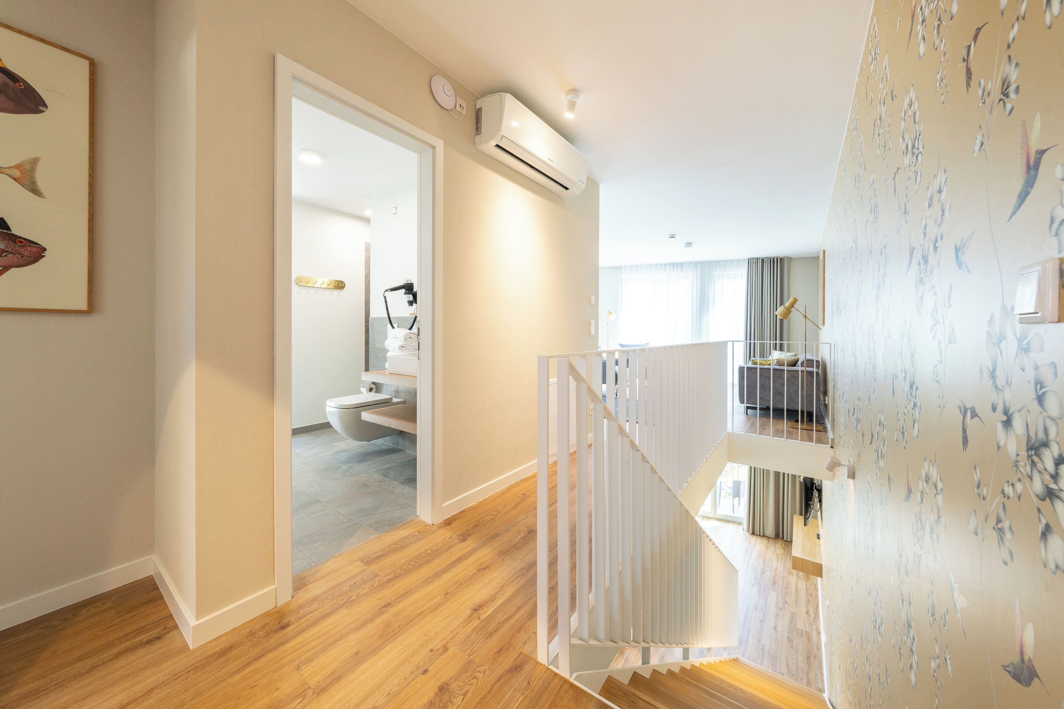 A modern interior with a wooden floor, a staircase, and a bathroom visible through an open door.