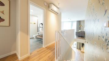 A modern interior with a wooden floor, a staircase, and a bathroom visible through an open door.