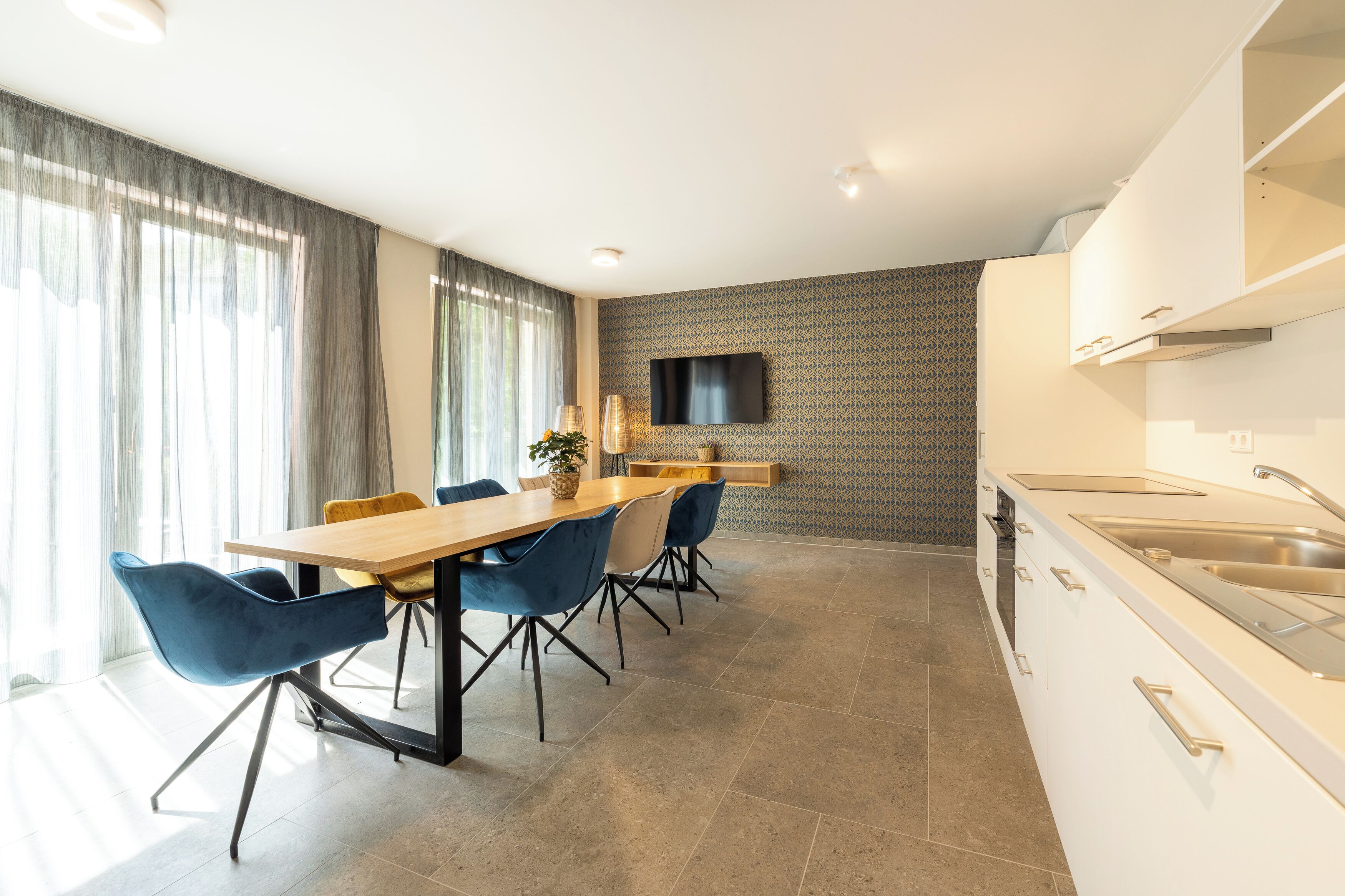 A modern kitchen with a dining area, a flat-screen TV mounted on the wall, and a built-in oven.