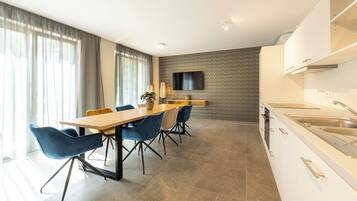 A modern kitchen with a dining area, a flat-screen TV mounted on the wall, and a built-in oven.