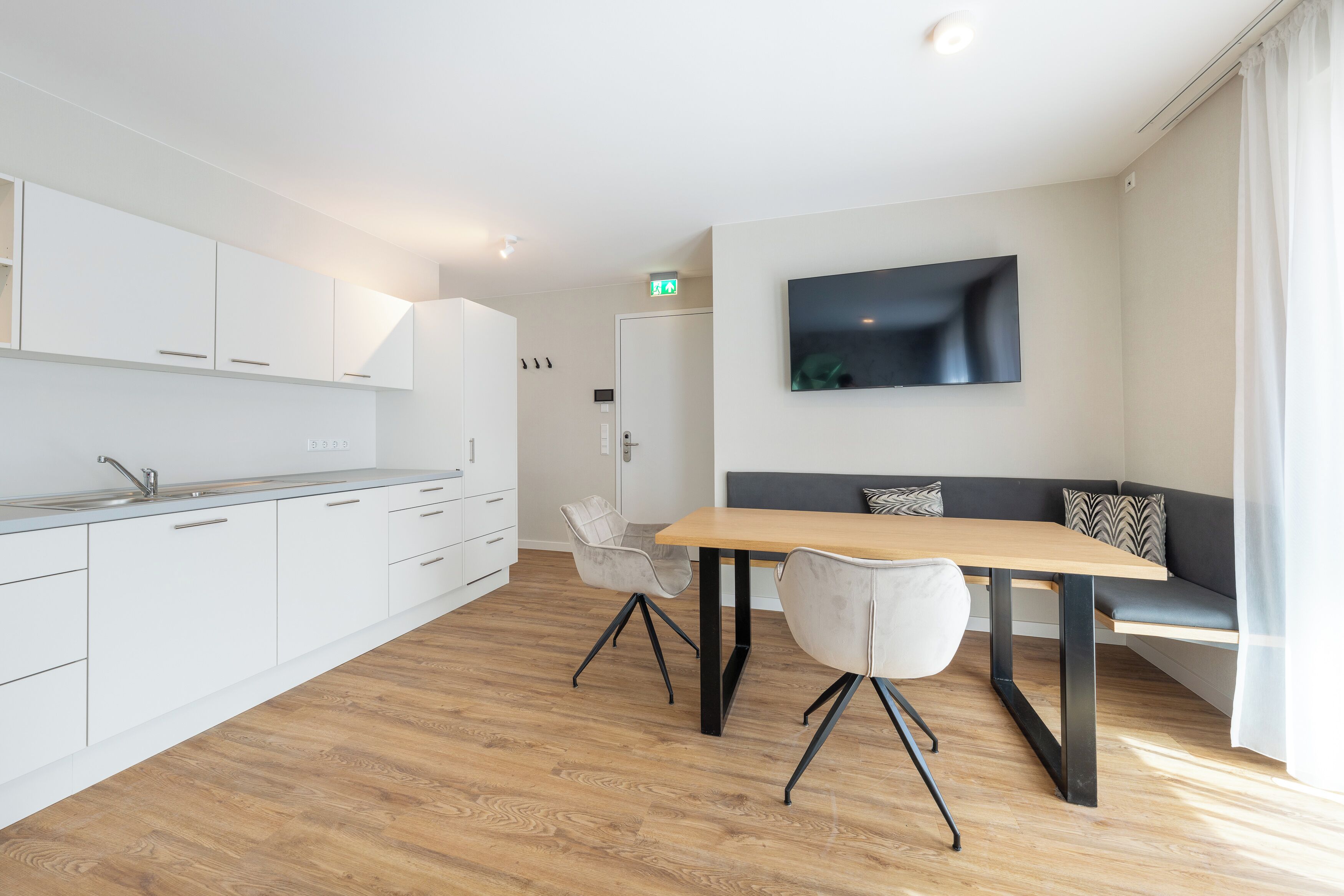 Una cocina moderna con armarios blancos, una mesa de comedor de madera y un sofá gris.