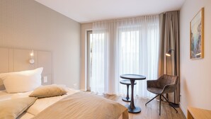 Una habitación de hotel con una cama, una silla, una mesita y un cuadro en la pared.