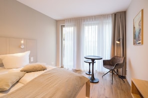 Una habitación de hotel con una cama, una silla, una mesita y un cuadro en la pared.