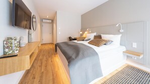 A modern bedroom with a bed, bedside table, TV, and a view of the hallway.
