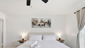 A neatly made bed with a quilted white duvet, two pillows, and rolled towels on a wooden nightstand. A painting is hung on the wall above the bed. - Large 2 Bed Lower Greenville Getaway (Right Side) (Dallas)