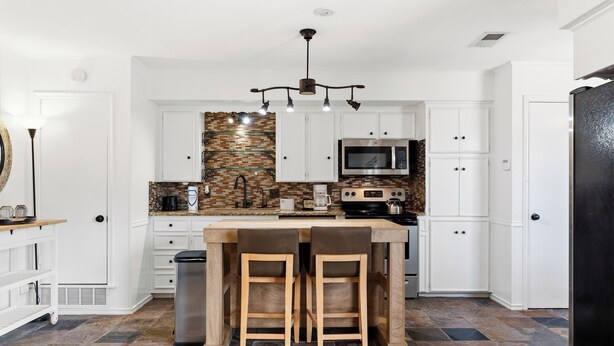 A kitchen with white cabinets, a central island with stools, a microwave, and a stove. - Large 2 Bed Lower Greenville Getaway (Right Side) (Dallas)