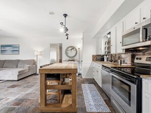 A modern kitchen with a wooden island, stainless steel appliances, and a dining area with a sofa and a lamp.