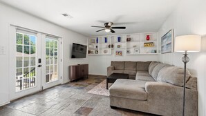 A living room with a grey sofa, a TV mounted on the wall, a ceiling fan, and a floor lamp. - Large 2 Bed Lower Greenville Getaway (Right Side) (Dallas)