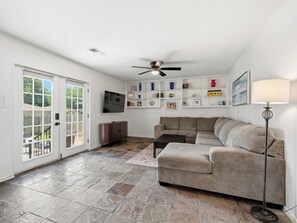 A living room with a grey sofa, a TV mounted on the wall, a ceiling fan, and a floor lamp.