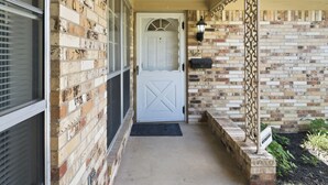 A covered porch with a brick wall, a white door, and a black mailbox. - Large 2 Bed Lower Greenville Getaway (Right Side) (Dallas)