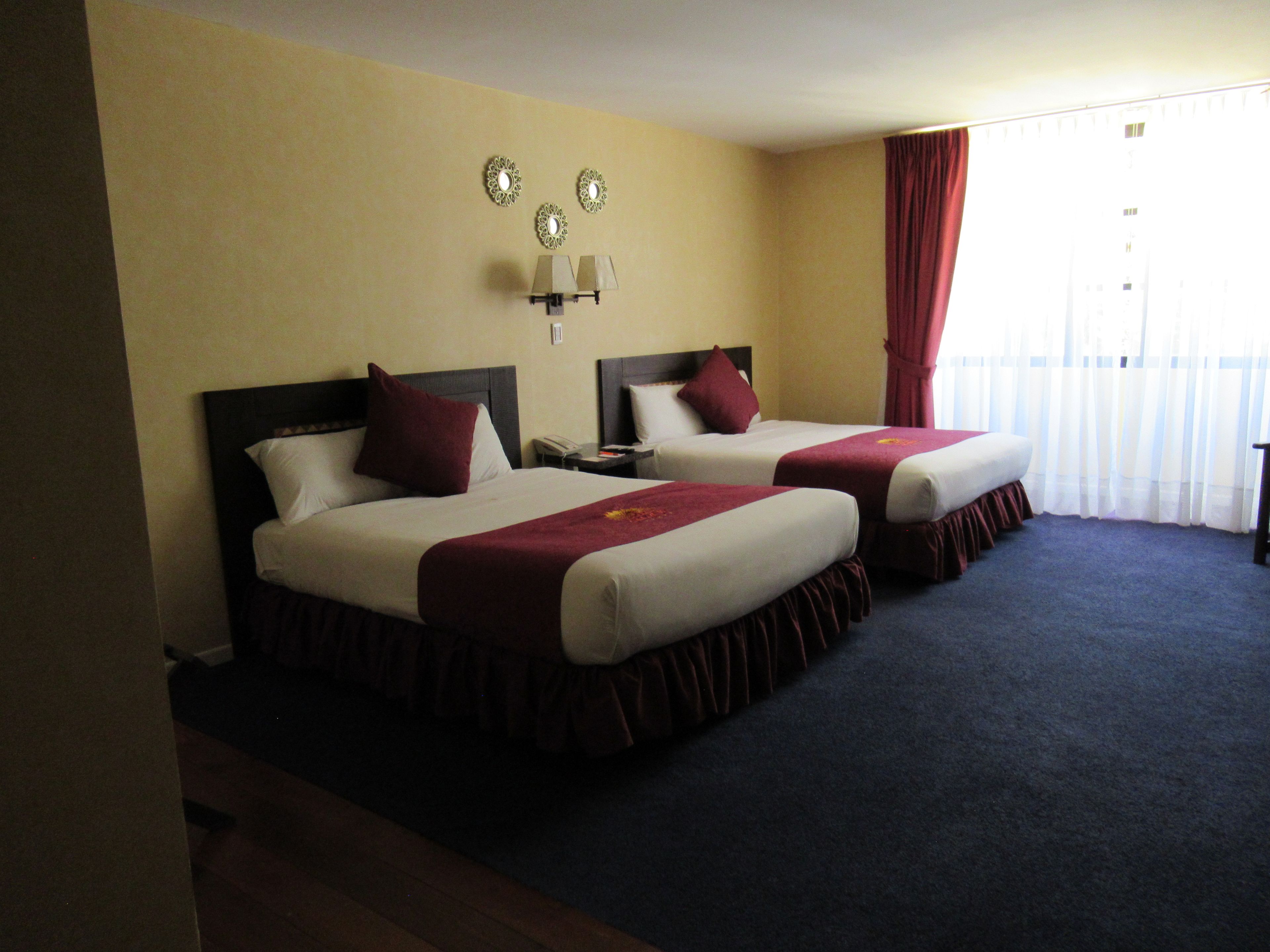 Una habitación de hotel con dos camas, una mesita de noche, una lámpara y una ventana con cortinas.