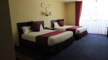 Una habitación de hotel con dos camas, una mesita de noche, una lámpara y una ventana con cortinas.