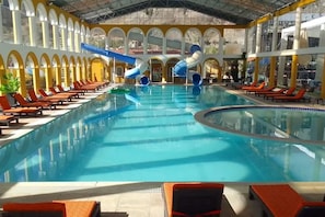 A large indoor swimming pool with a water slide, sun loungers, and a covered area with arches. - HOTEL RESORT SALQUIS (La Paz)