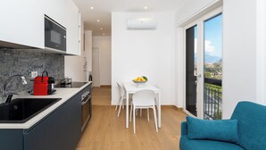 A modern kitchen with a built-in microwave, a red kettle, and a sink. There is a dining area with a white table and chairs, and a balcony with a view. - YourHome - Il Nido Apartments  (Sant'Agnello)