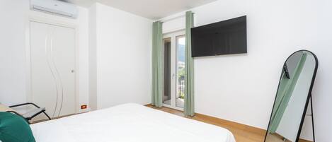 A bedroom with a bed, a TV, a mirror, and a sliding door to a balcony.