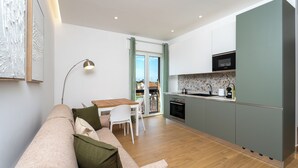 A modern kitchen with a dining area, a sofa with cushions, and a view through a glass door. - YourHome - Il Nido Apartments  (Sant'Agnello)