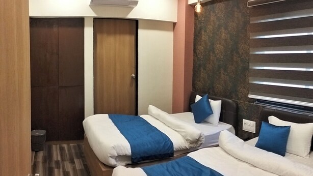A hotel room with two beds, a ceiling fan, an air conditioning unit, and a window with blinds. - Hotel Krishna Inn (Ahmedabad)
