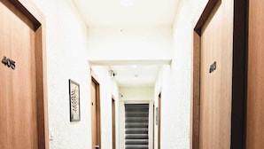 A hotel hallway with wooden doors, a tiled floor, and a staircase leading to an upper floor. - Hotel Krishna Inn (Ahmedabad)