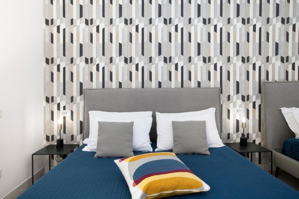 Una habitación de hotel con una cama, dos mesitas de noche y un papel tapiz estampado.
