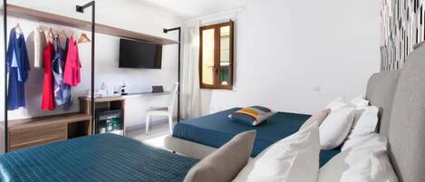 A hotel room with two beds, a desk, a TV, and a wardrobe with hanging clothes.