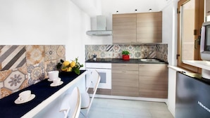 Eine kleine Küche mit dunkler Arbeitsplatte, weißen Stühlen, einem Holzschrank und einem Kühlschrank.