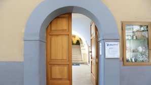 Ein rundbogiges Portal führt zu einer Treppe, einer Holztür und einem Schild.