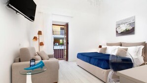 Ein modernes Hotelzimmer mit einer Couch, einem Glastisch, einem Bett mit blauer Bettdecke, einem an der Wand montierten Fernseher und einem Gemälde über dem Bett.