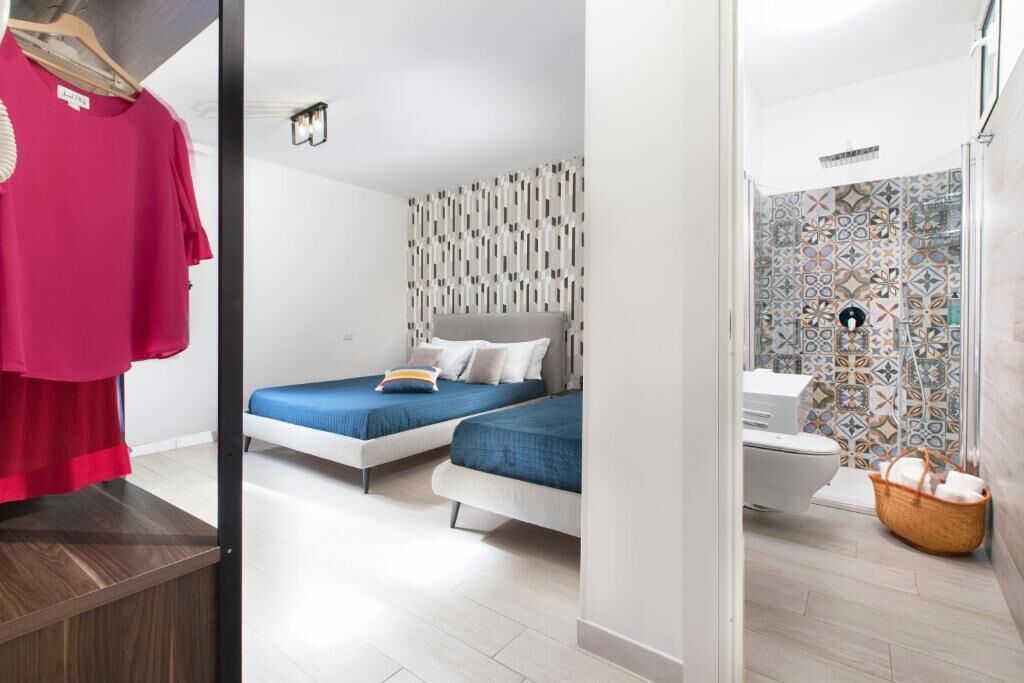 Una habitación de hotel moderna con dos camas, un baño con baldosas estampadas y suelo de madera.