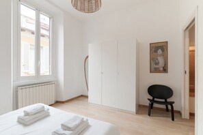 Ein Schlafzimmer mit Bett, Heizkörper, Kleiderschrank, Stuhl und einem Bild an der Wand.