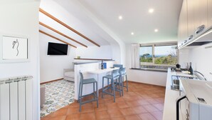 A modern kitchen with a dining area, a TV mounted on the wall, and a window with a view. - YourHome - Jolly Pini (Sant'Agnello)