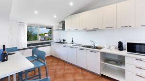 A modern kitchen with white cabinets, a dining table with chairs, a window with curtains, and a view of greenery outside. - YourHome - Jolly Pini (Sant'Agnello)