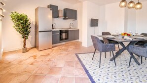 Una cocina moderna con electrodomésticos integrados, un comedor con mesa y sillas, y una planta en maceta.
