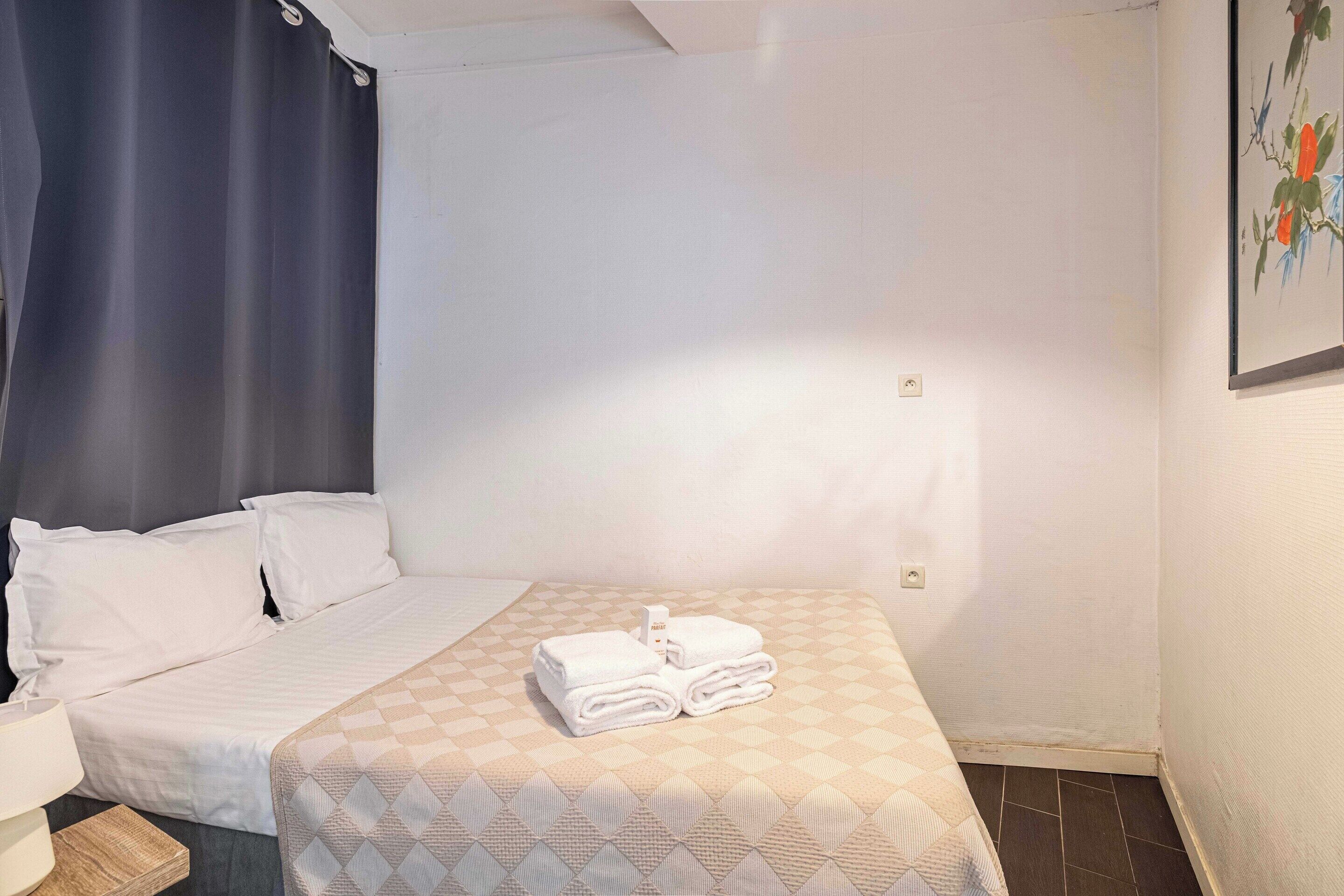 Quarto de hotel com cama, mesa de cabeceira, abajur e um quadro na parede.