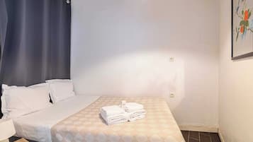 Quarto de hotel com cama, mesa de cabeceira, abajur e um quadro na parede.