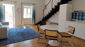 A modern living room with a dining table, chairs, a staircase, and a kitchen area. - YourHome - La Maddalena Blue House (La Maddalena)