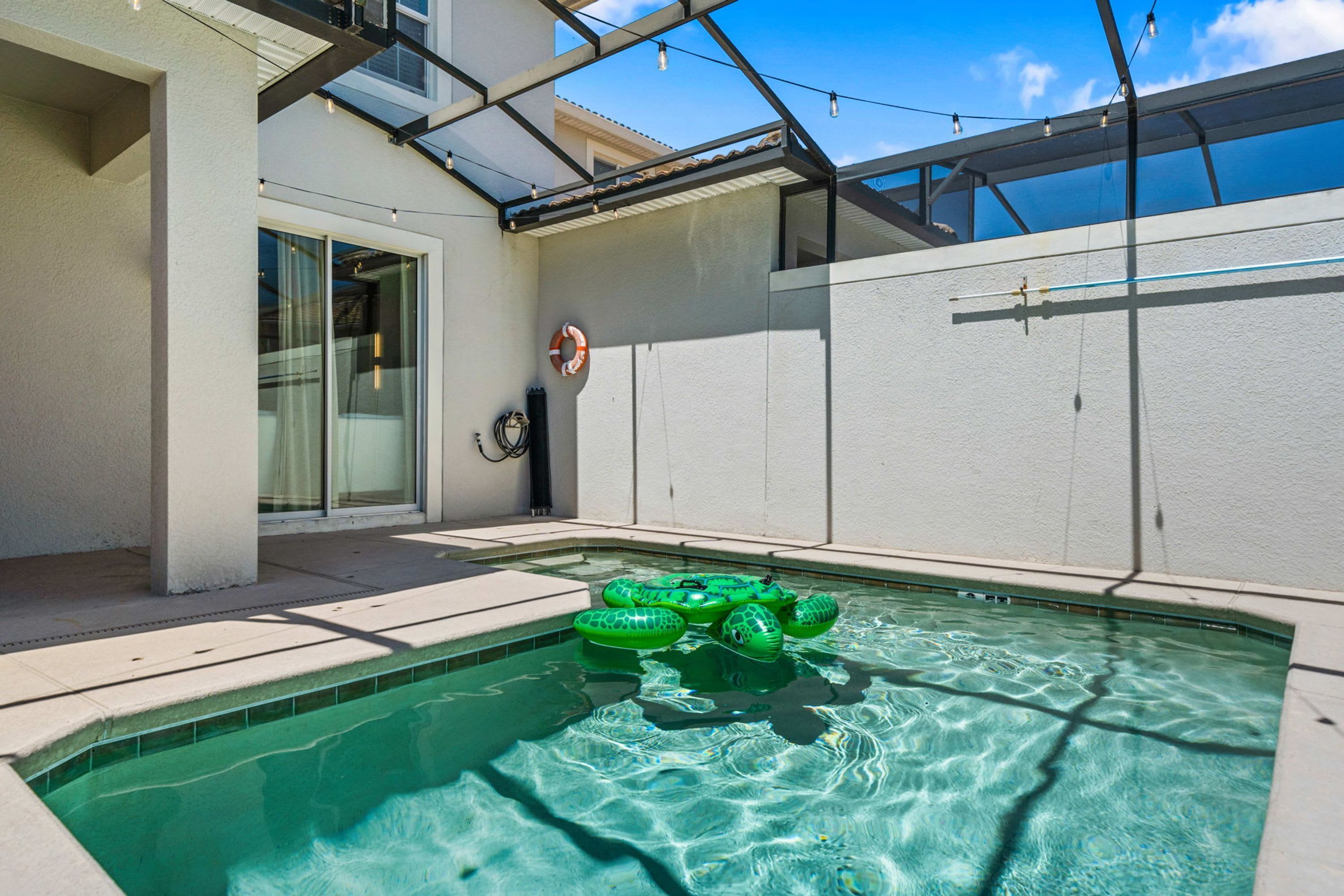 A swimming pool with inflatable rings, a glass door entrance, and a clear sky.
