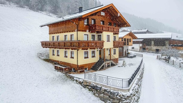 Un chalet de varios pisos con un balcón, un muro de piedra de contención y un paisaje cubierto de nieve.