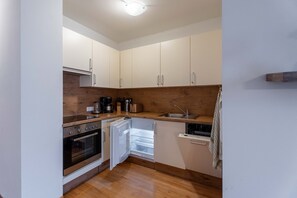 A compact kitchen with white cabinets, a built-in oven, and a dishwasher. - Weitblick Appartements - 1 (Bad Hofgastein)