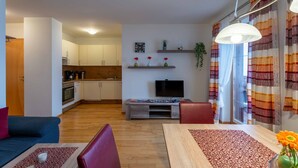 Una sala de estar moderna con sofá, mesa de comedor, televisor y cocina al fondo.