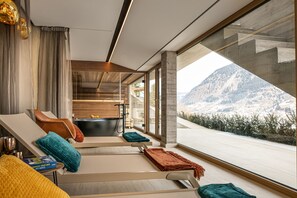 A modern spa room with a large window, a bathtub, and a lounge area with towels and a book. - Apartments VIU - 03 Great VIU (Bad Hofgastein)