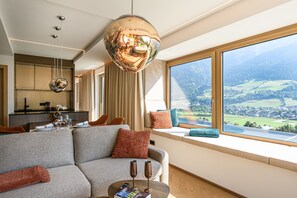 Ein modernes Wohnzimmer mit einer Couch, einem Esstisch, einem großen Fenster mit Landschaftsblick und einer außergewöhnlichen, kugelförmigen Lampe.